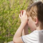 Young boy in white shirt gazes thoughtfully by stained glass window