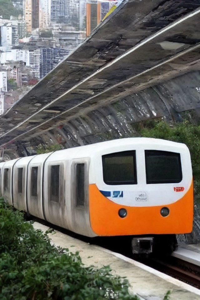 Orange and white train emerges from tunnel in lush greenery with city buildings in background