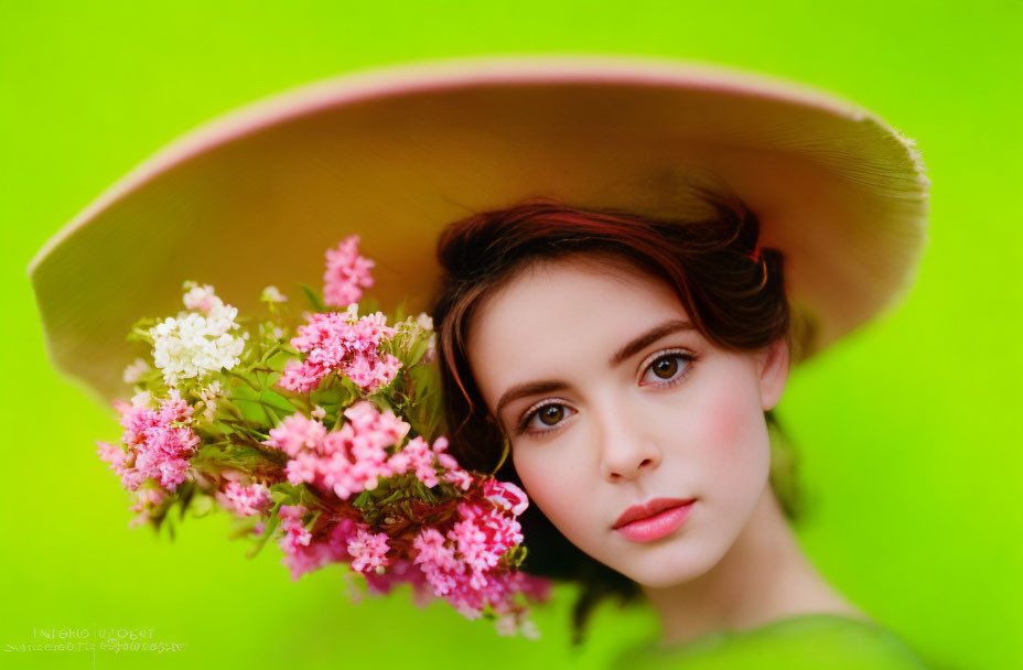 Woman in wide-brimmed hat holding pink flowers on vibrant green background