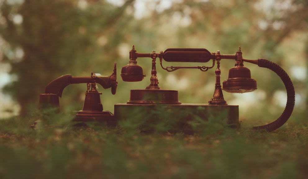 Vintage rotary dial telephone on grass with blurred greenery background