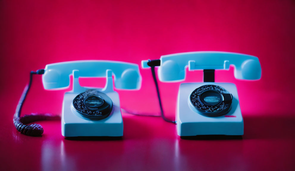 Vintage telephones on red background: one off-hook, receiver lifted.