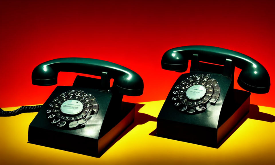 Vintage rotary dial telephones on yellow surface with lifted handset