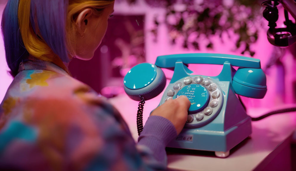 Woman dialing retro blue rotary phone under pink lighting