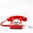 Vintage red rotary dial telephone off the hook on white background