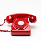 Vintage red rotary dial telephone off the hook on white background