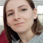 Fair-skinned woman in grey sweater takes selfie with light brown hair and makeup.