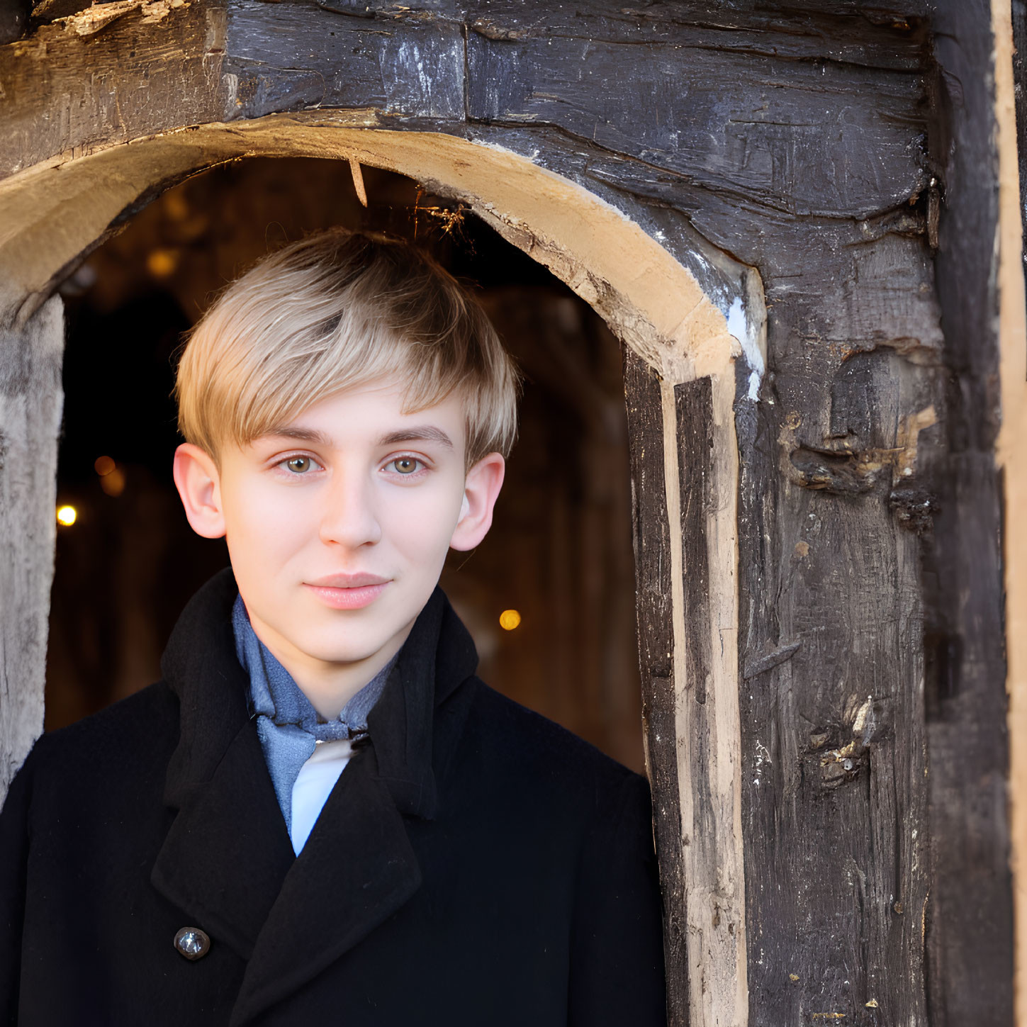 Young person with light hair and blue eyes in dark coat at rustic wooden doorway