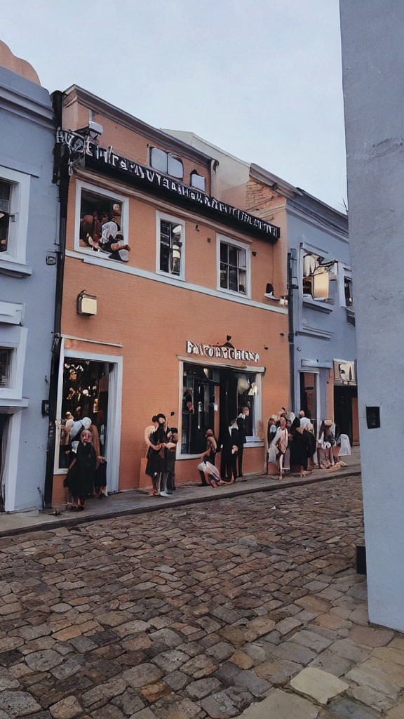 People waiting in line outside "Taylor Taylor" building on cobblestone street with balcony above