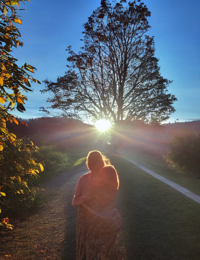 Embracing couple on path at sunset with tree silhouette