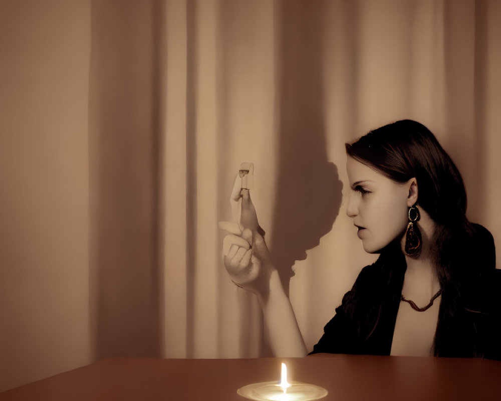 Woman sitting at table with lit candle and extinguished matchstick, casting shadow on draped background.