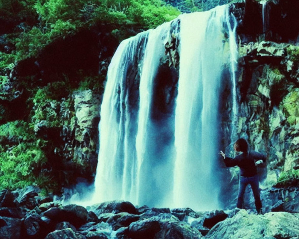 Person photographing majestic waterfall in lush greenery