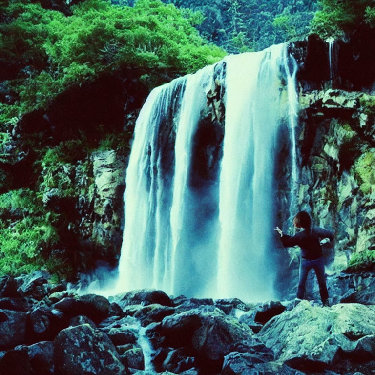 Person photographing majestic waterfall in lush greenery