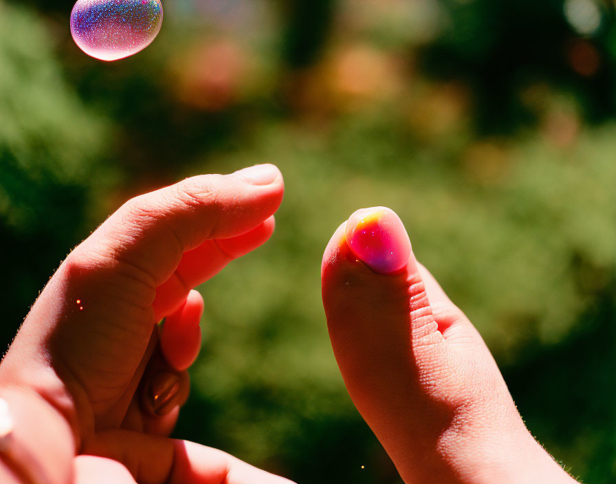 Fingers near bubble in sunlight with green background