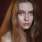 Young woman portrait with blue eyes, wavy hair, delicate necklace, dark background