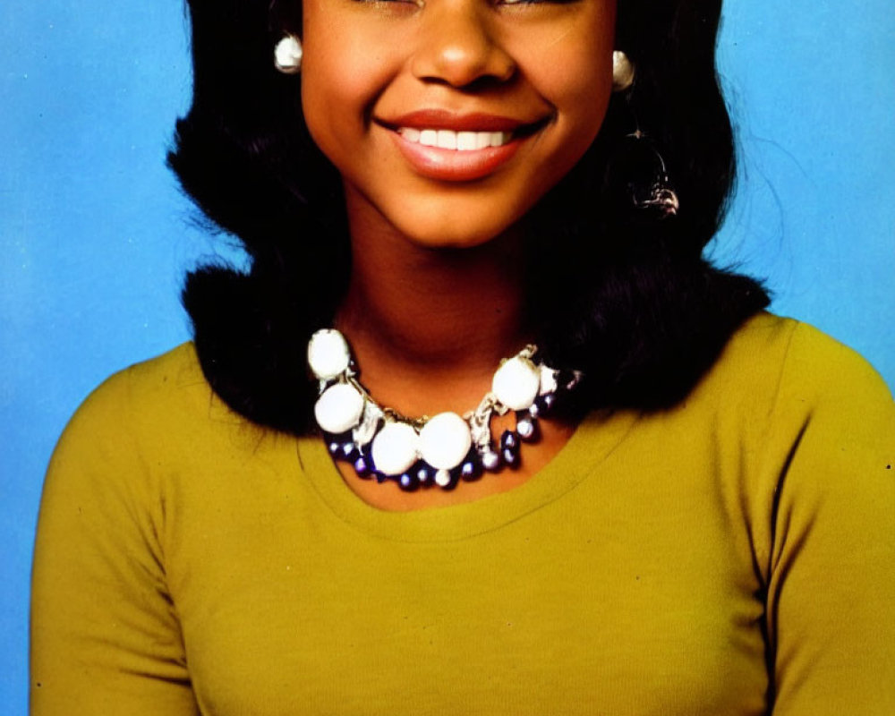 Smiling woman with hoop earrings and mustard top on blue background