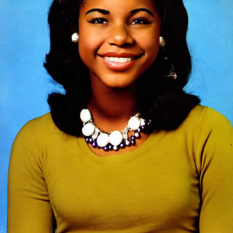 Smiling woman with hoop earrings and mustard top on blue background