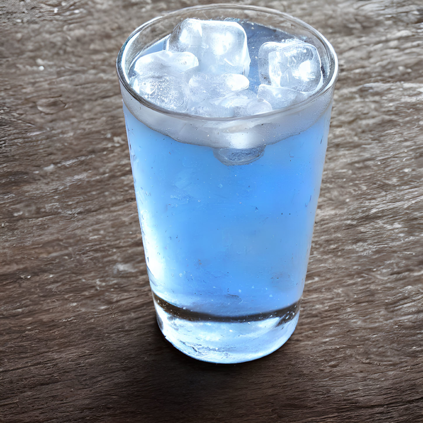 Blue liquid in glass with ice cubes on wooden surface