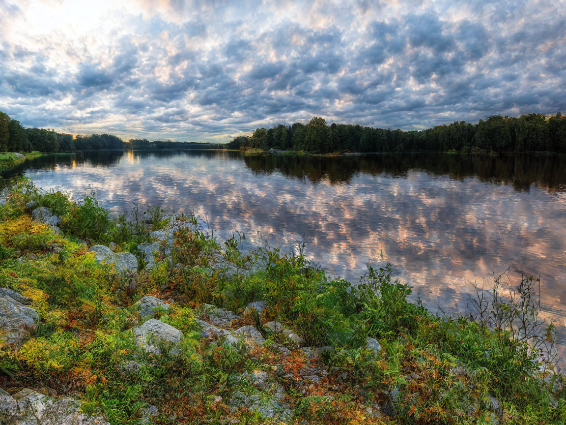 Tranquil river scene with cloudy sky, lush trees, and rocky shoreline