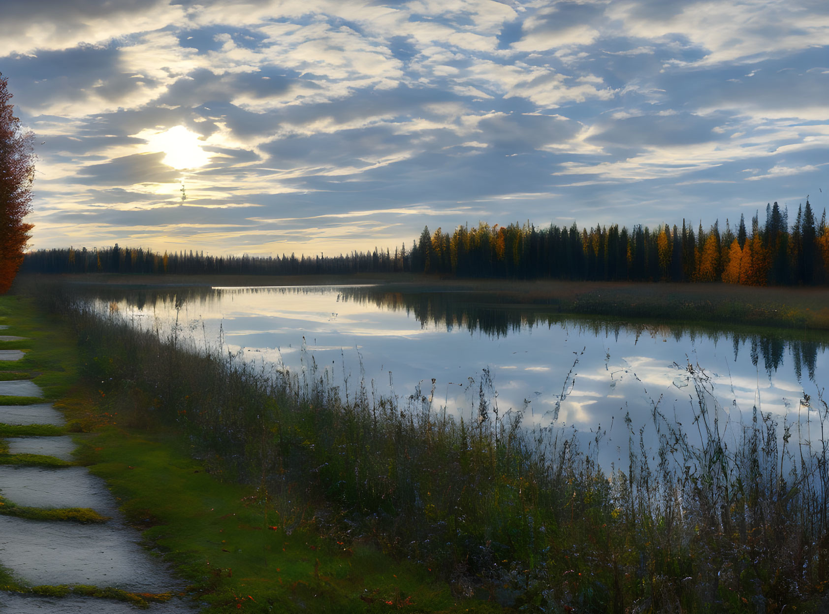 Tranquil sunset scene with lake, autumn trees, and footpath