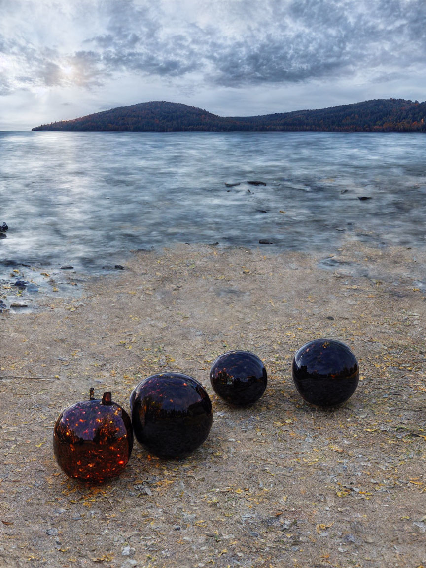 Dark Spherical and Cubic Objects on Lakeshore with Forested Hill and Cloudy Sky at