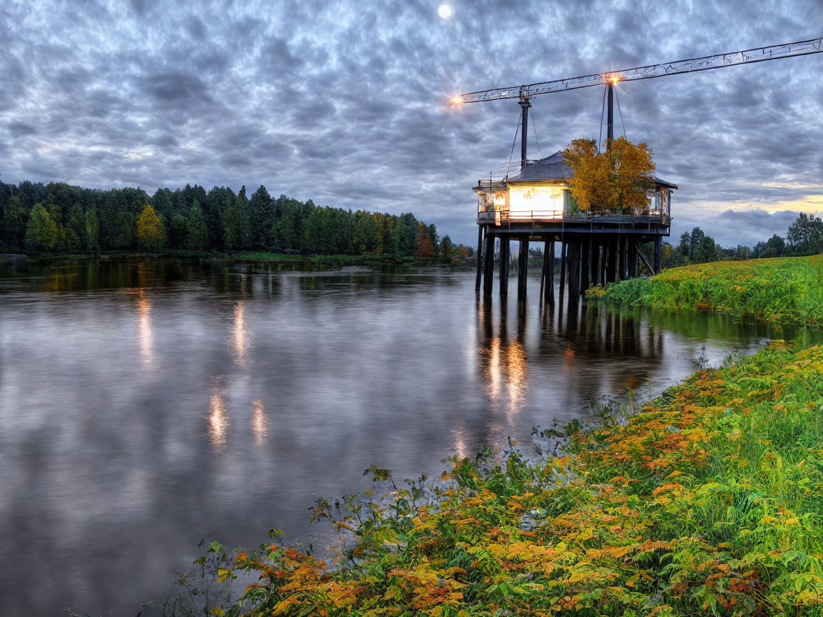 Tranquil river at dusk with reflections, stilt structure, crane, trees, and cloudy sky