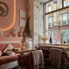 Person seated in pink-themed cafe corner with plants and framed pictures