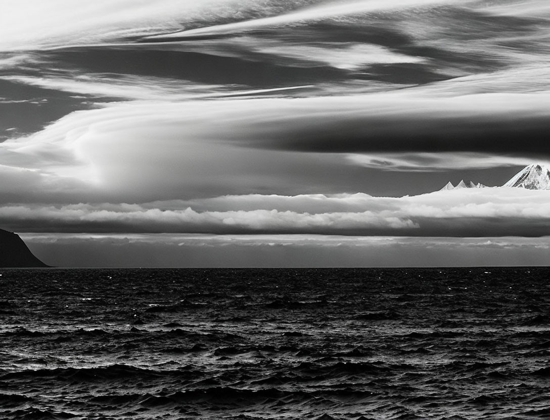 Monochromatic seascape with textured clouds, rough waves, and distant mountains