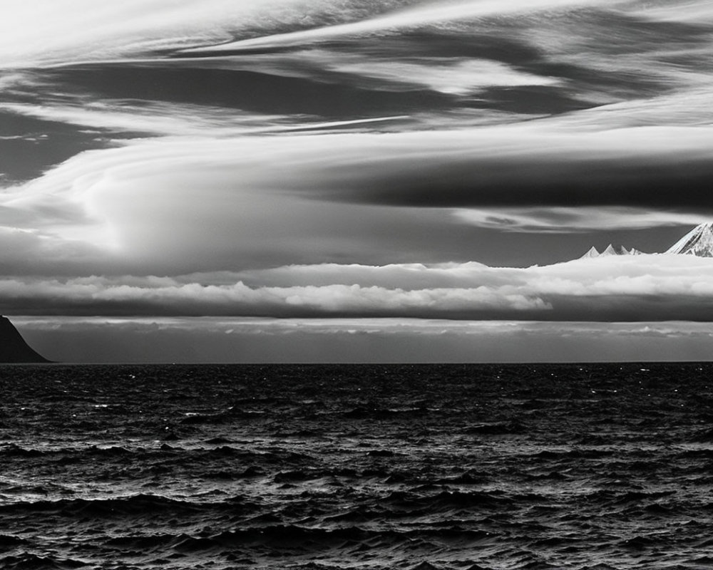 Monochromatic seascape with textured clouds, rough waves, and distant mountains