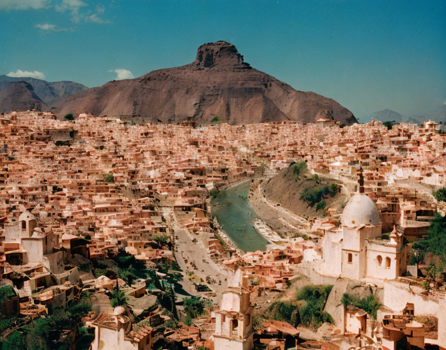 Urban buildings cluster near river, hill backdrop, blue sky with scattered clouds.