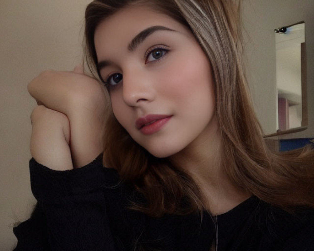 Young woman with fair skin and dark hair in black top and pendant necklace poses with hand on chin