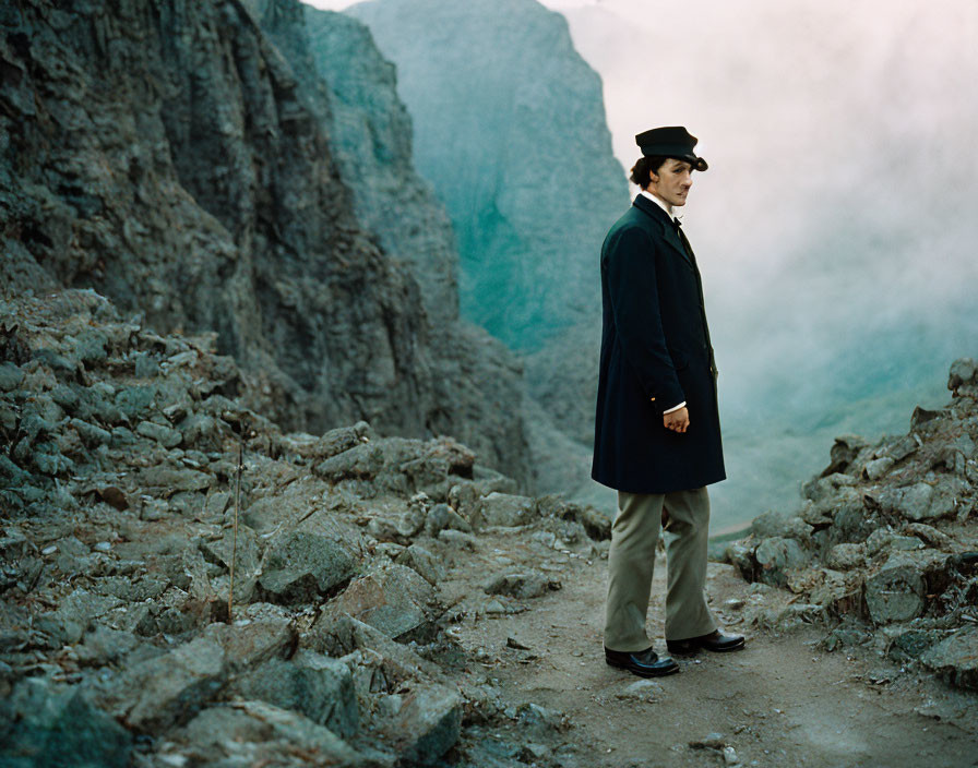 Vintage Suit and Hat Man in Rocky Terrain with Mountains and Misty Background