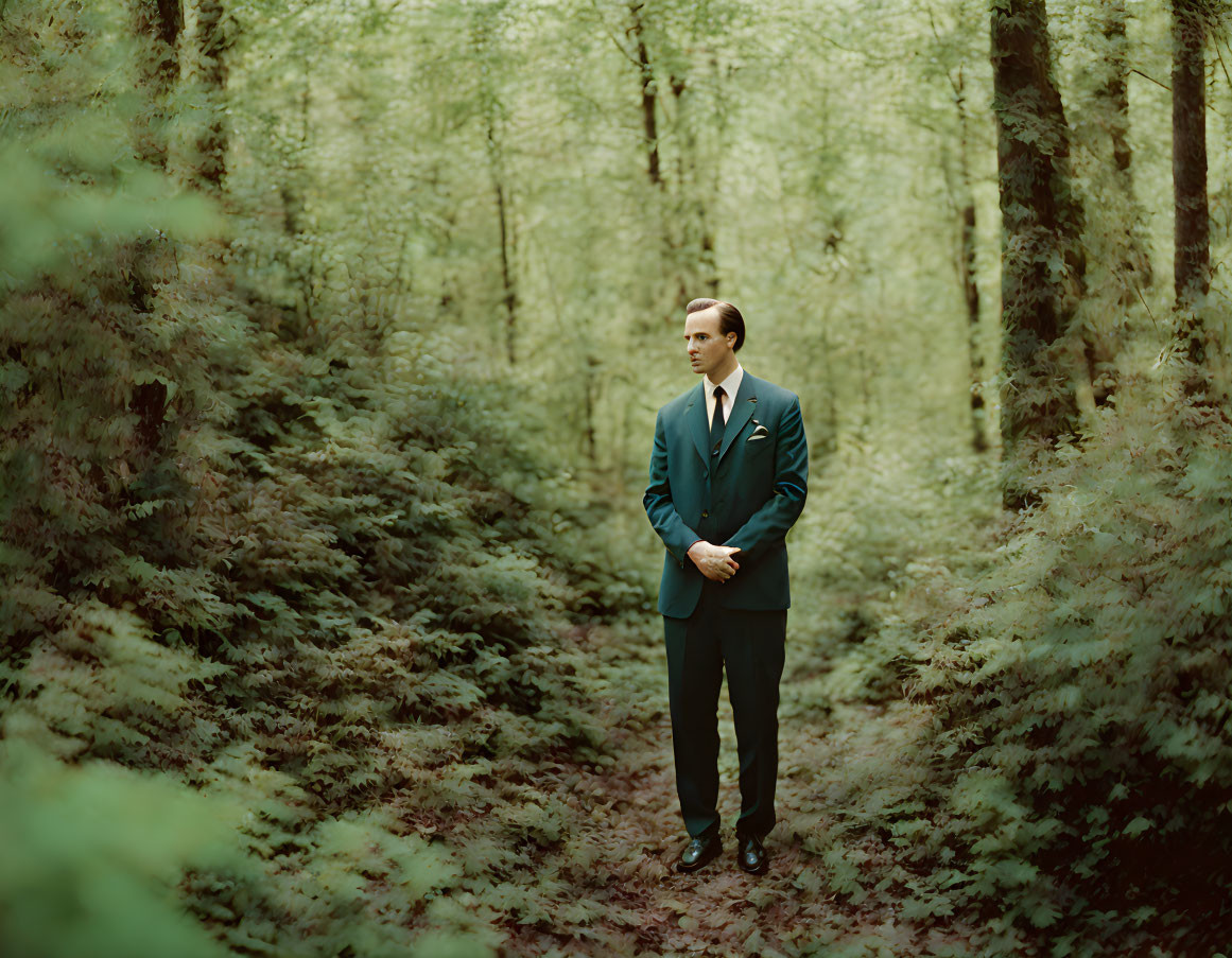 Man in dark suit standing in lush green forest with sunlight filtering through trees