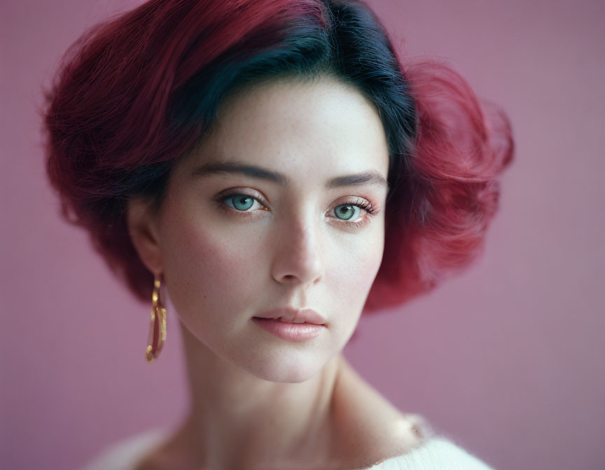 Woman with red and teal hair and green eyes on pink background.