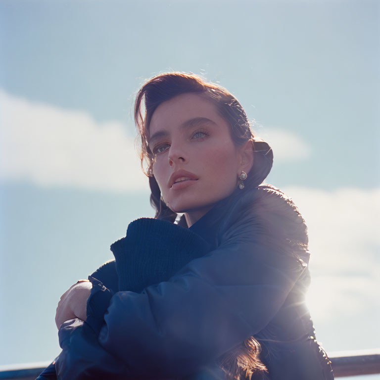 Dark-haired woman in dark jacket gazes under bright sky