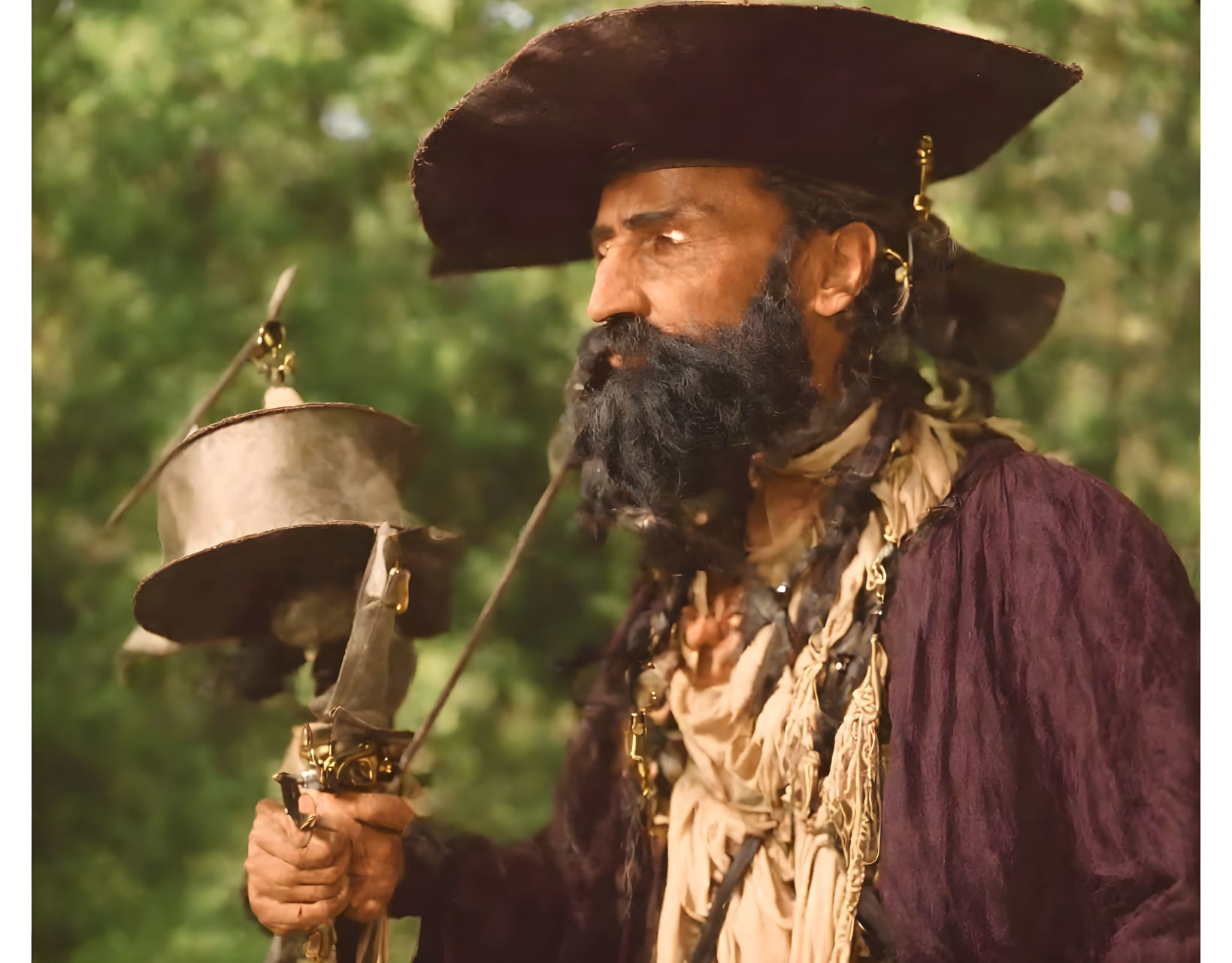 Man in pirate costume with tricorn hat, beard, and sword in hand against natural background