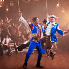 Men in blue and gray costumes swinging on ropes in a smoky stage setting