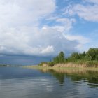 Tranquil lake landscape with lush green trees and dramatic sky