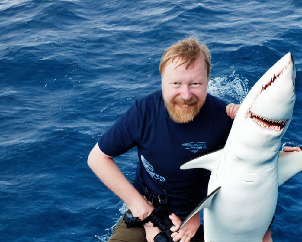 Bearded man smiling with toy shark over blue water