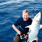 Bearded man smiling with toy shark over blue water