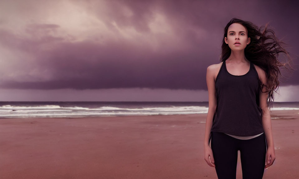 Woman with flowing hair on beach under stormy clouds.