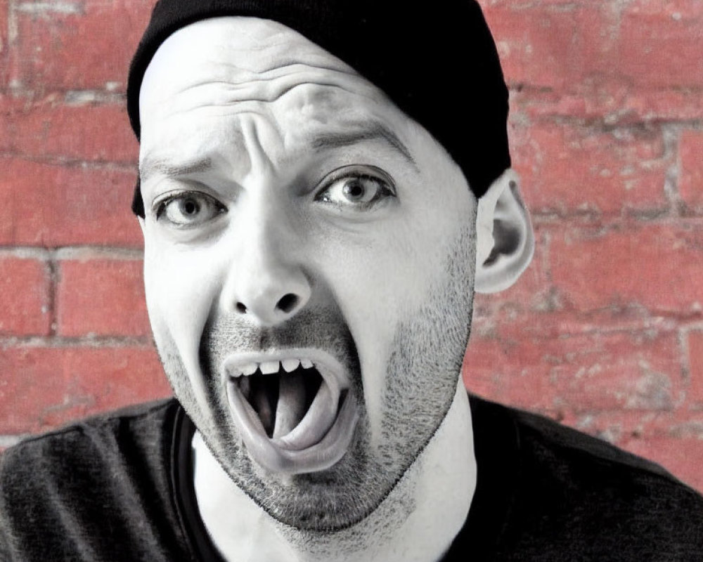 Surprised man in black beanie and T-shirt against red brick wall