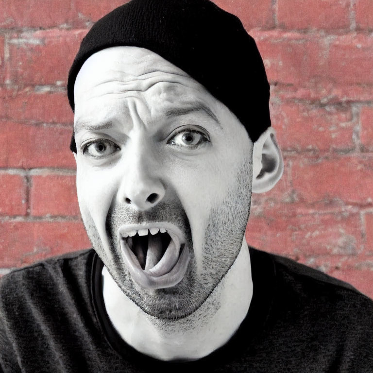 Surprised man in black beanie and T-shirt against red brick wall