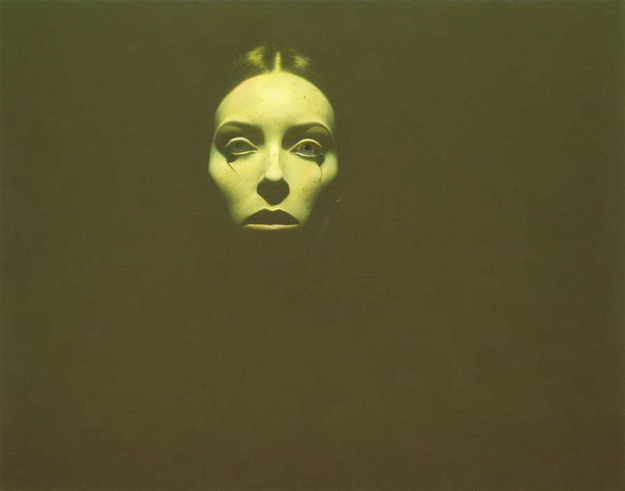 Mask-like face with hollow eyes and mouth on dark green background