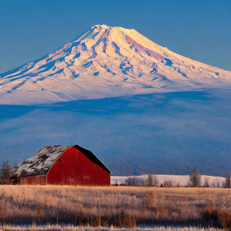 Red barn in snow-covered plain with snow-capped mountain and clear blue sky