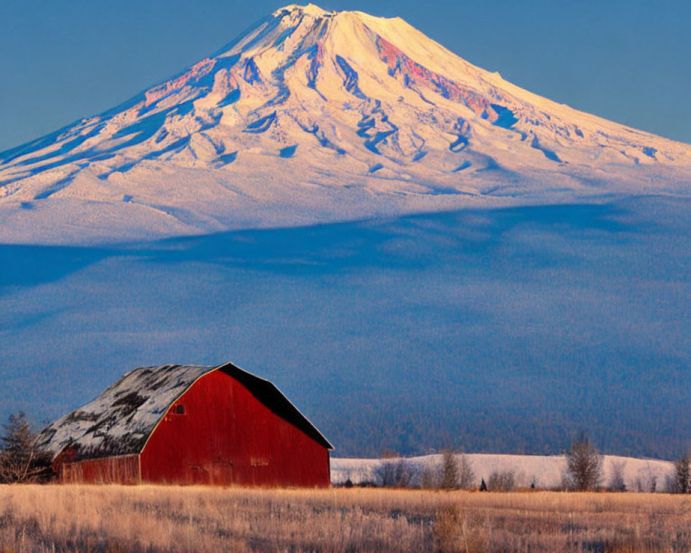 Red barn in snow-covered plain with snow-capped mountain and clear blue sky