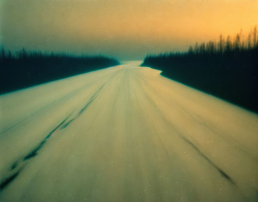 Snowy Road Flanked by Dark Forests Under Orange Sky