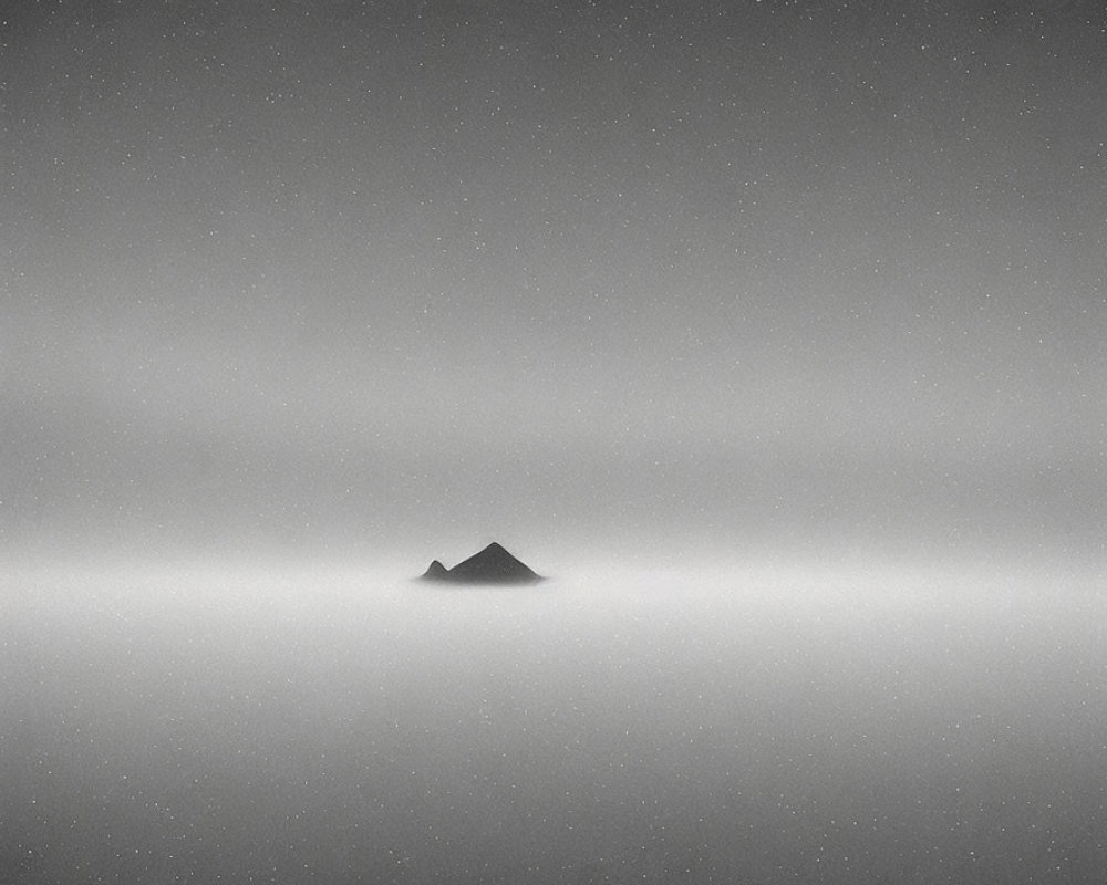 Mountain peak rises above sea of clouds in monochrome sky