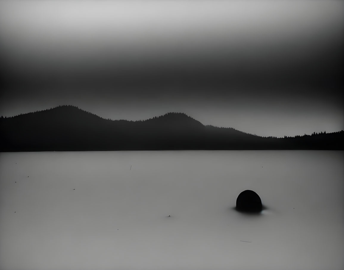 Monochromatic landscape with serene lake, rock, and silhouetted mountains