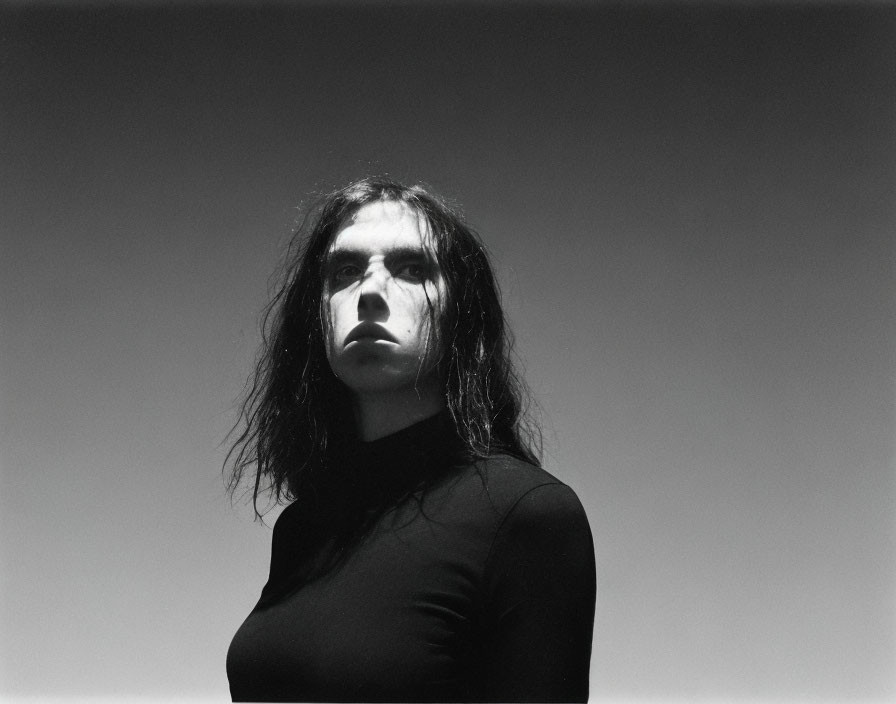 Portrait of person with long, dark hair in black top against gray background