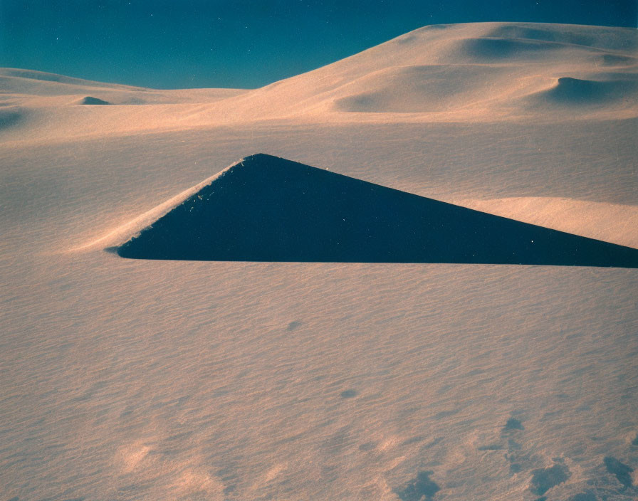 Snowy Landscape with Dark Triangular Shape in Soft Blue Sky